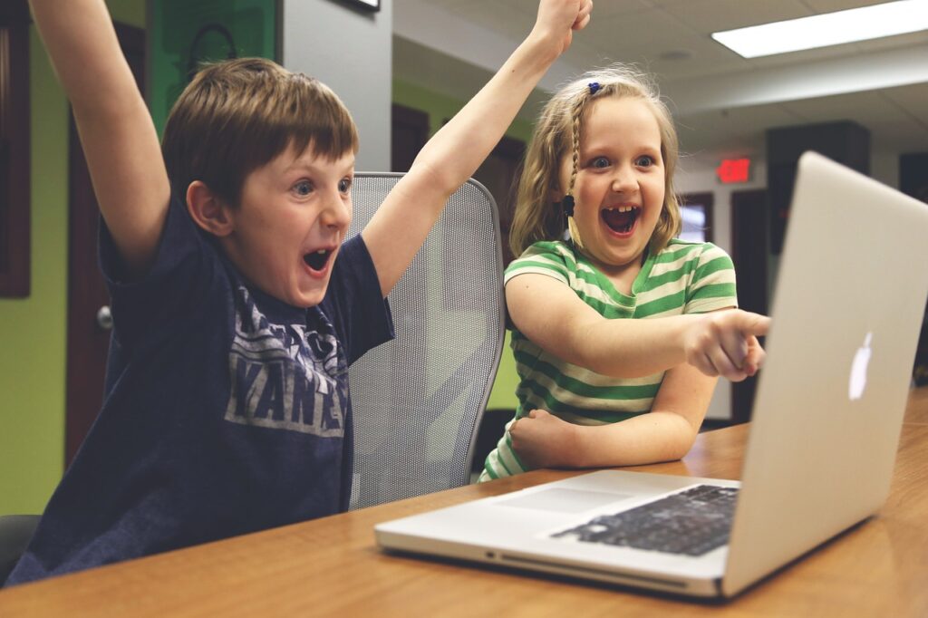 Two excited children looking at a laptop and interacting online.