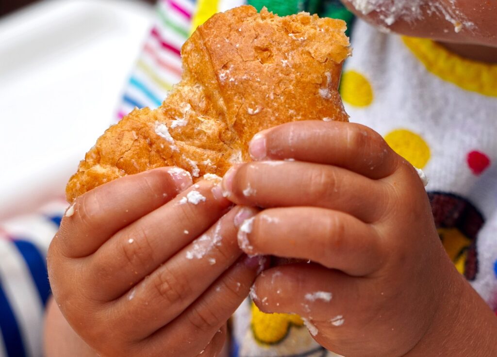 A close up of a child holding food with cream all over their hands and face